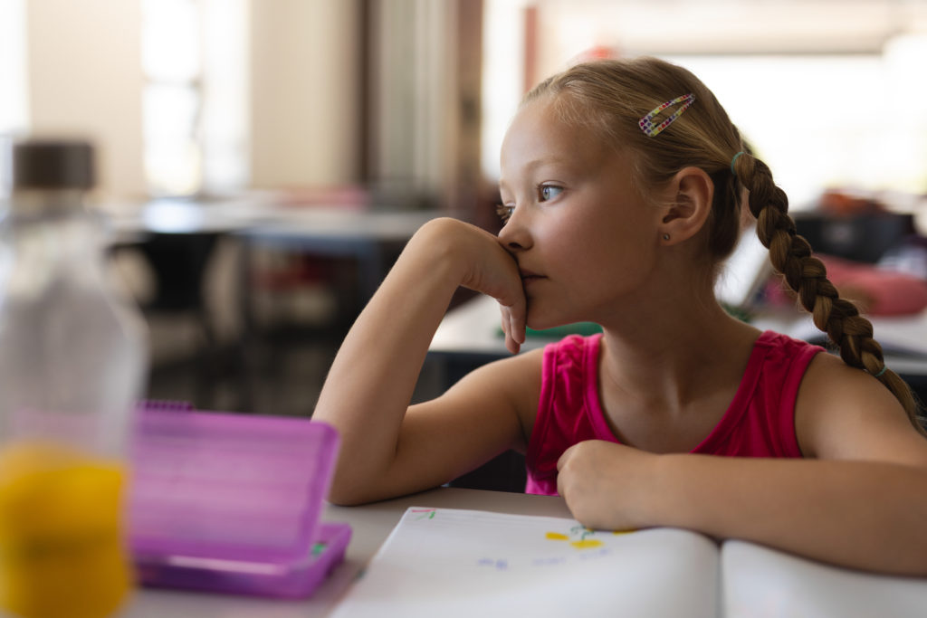 Close-up of distracted student leaning on desk and looking away in classroom of elementary school